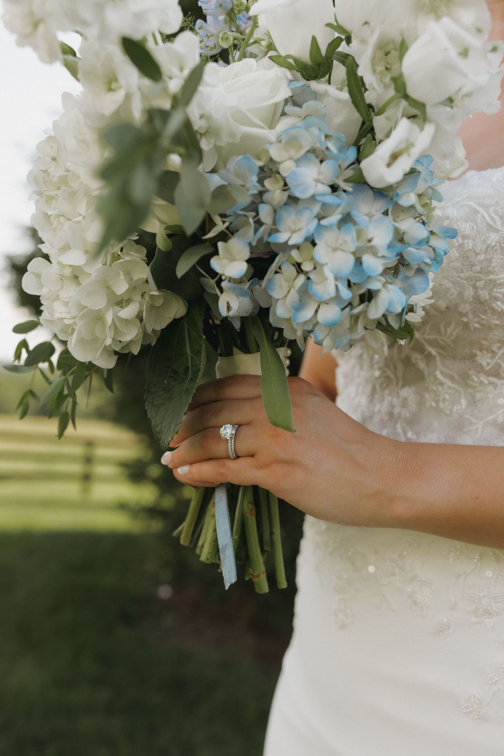 Bridal bouquet with white hydrangeas and delicate blue accents held against a white wedding dress.