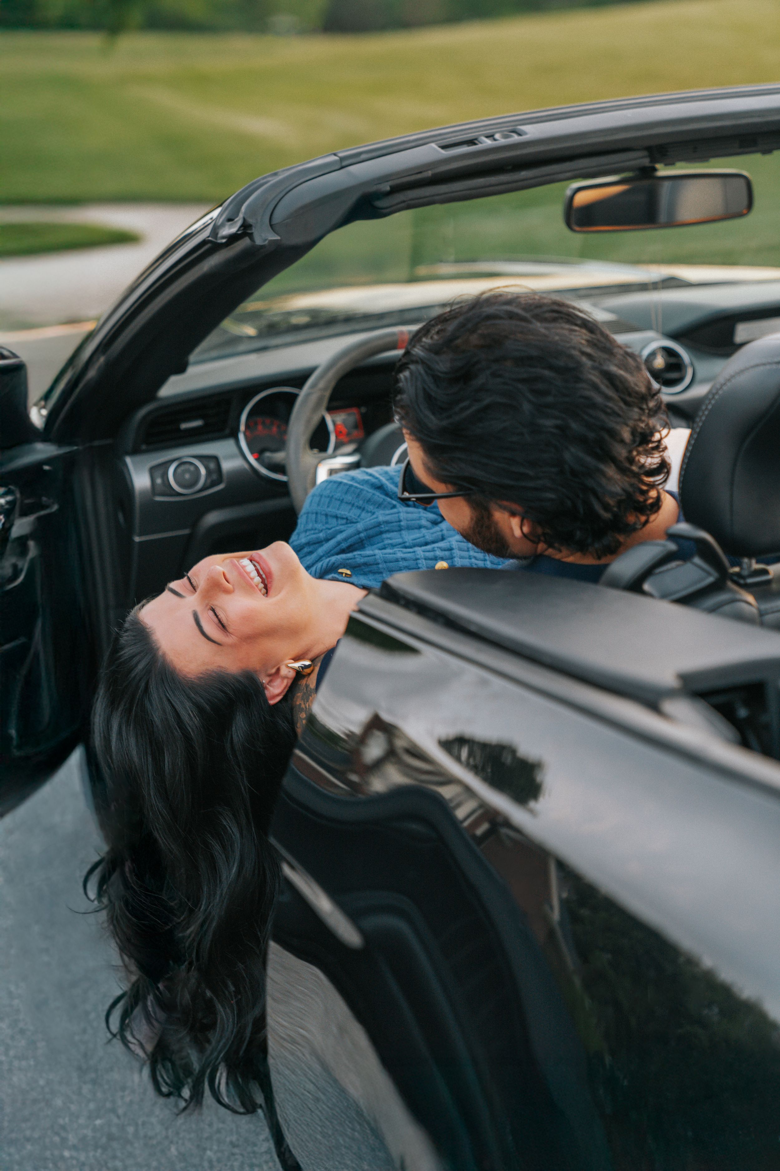 A person in a convertible car leans back dramatically with their long dark hair flowing in the wind.