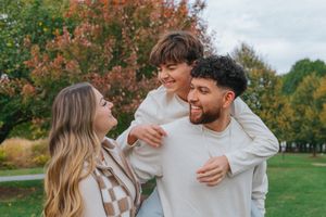A couple shares joyful moments together in a park during autumn with colorful fall foliage in the background.