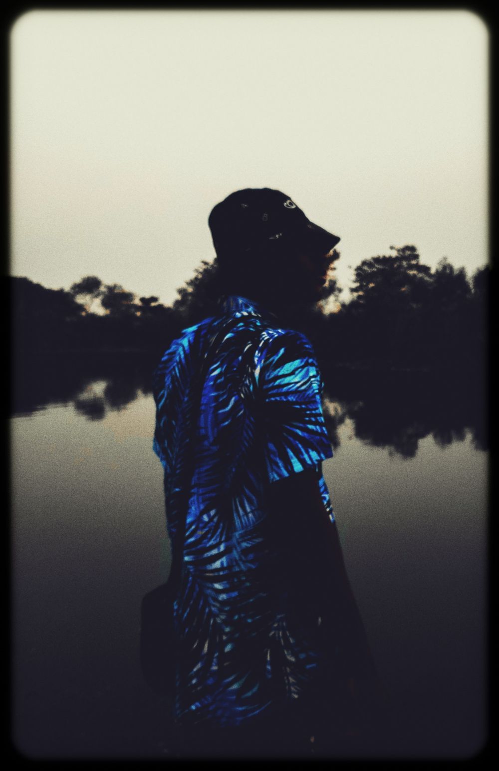 A silhouetted figure in a blue tropical print shirt stands against a moody gray sky in a series of artistic photographs.