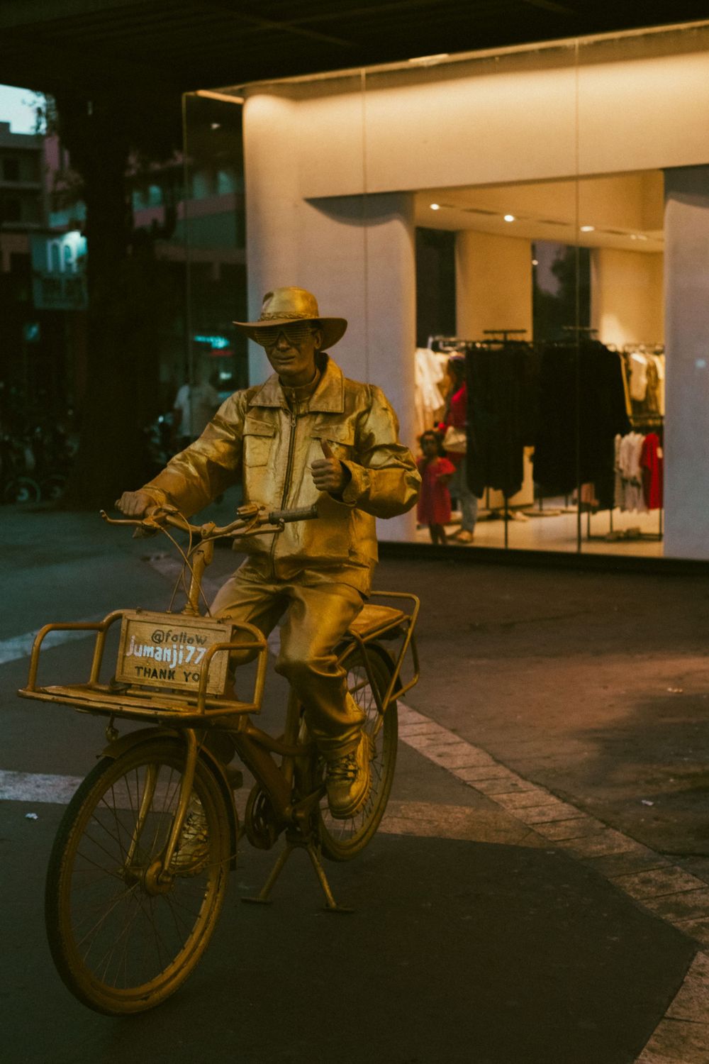 A motorcycle delivery person in a yellow uniform rides a vintage bicycle on a dimly lit street at night.