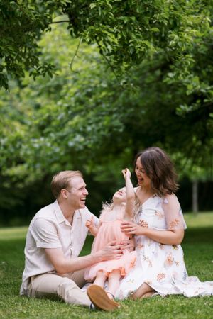 A happy family sharing laughter while sitting on grass under leafy trees.