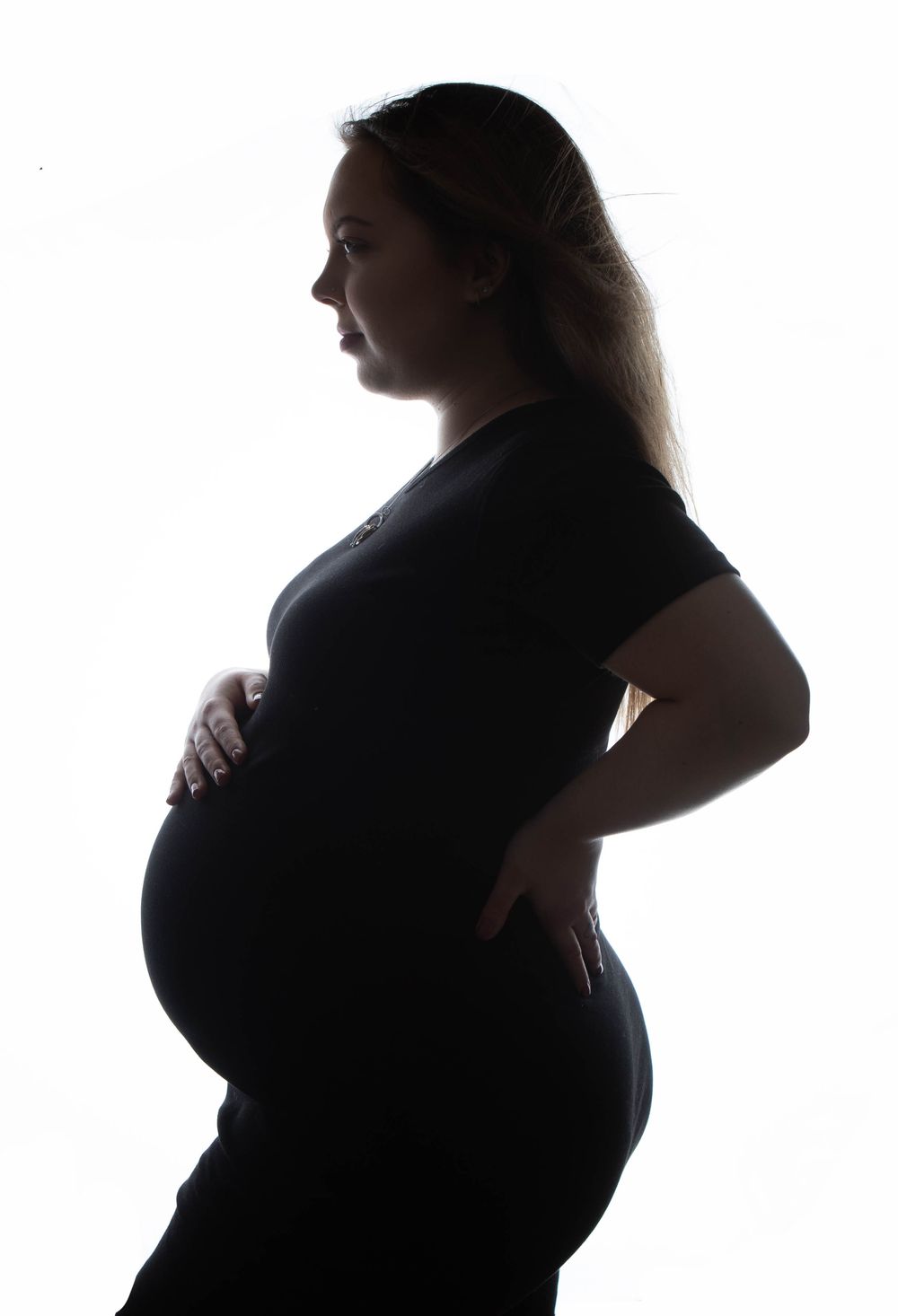Dramatic silhouette profile of pregnant woman in black dress cradling baby bump.