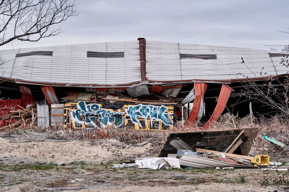 Abandoned collapsed building with colorful graffiti murals surrounded by debris and rubble under a cloudy sky.