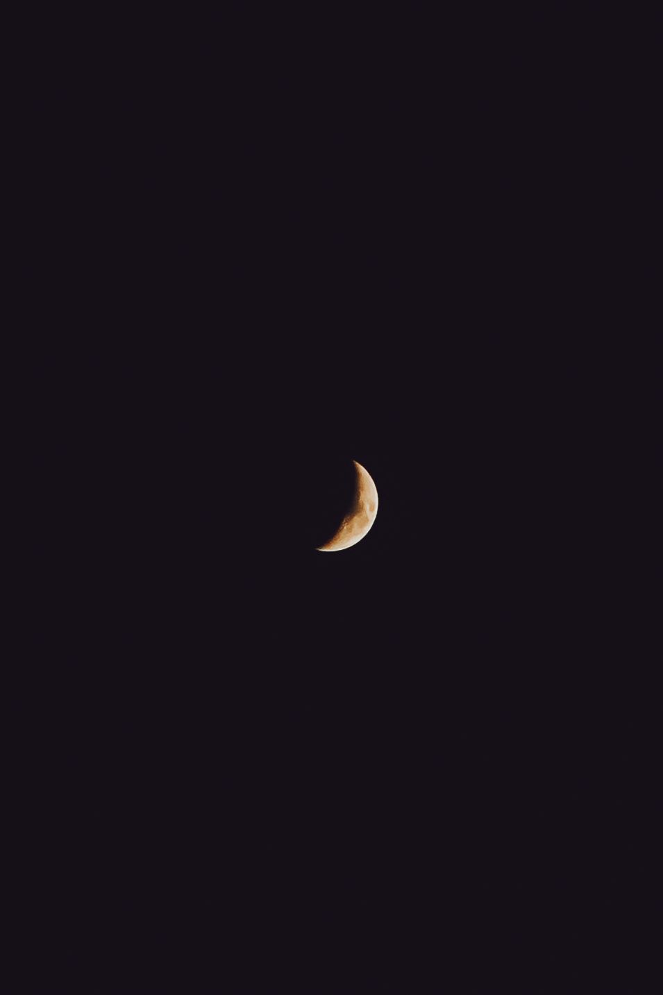 A crescent moon glows brightly against the dark night sky in a striking minimalist celestial photograph.