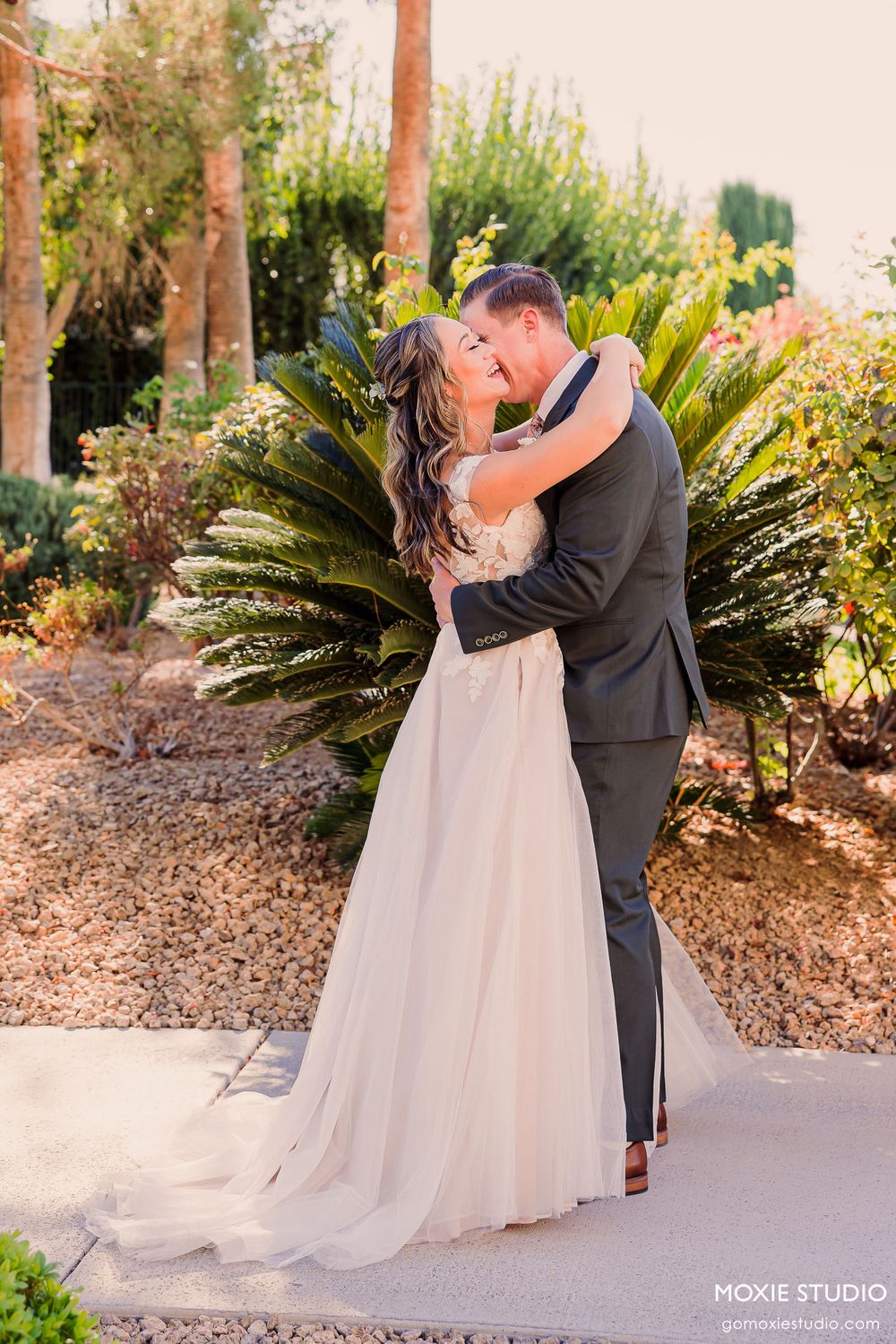 Romantic couple embraces and kisses in a garden setting with palm trees and lush greenery during golden hour.