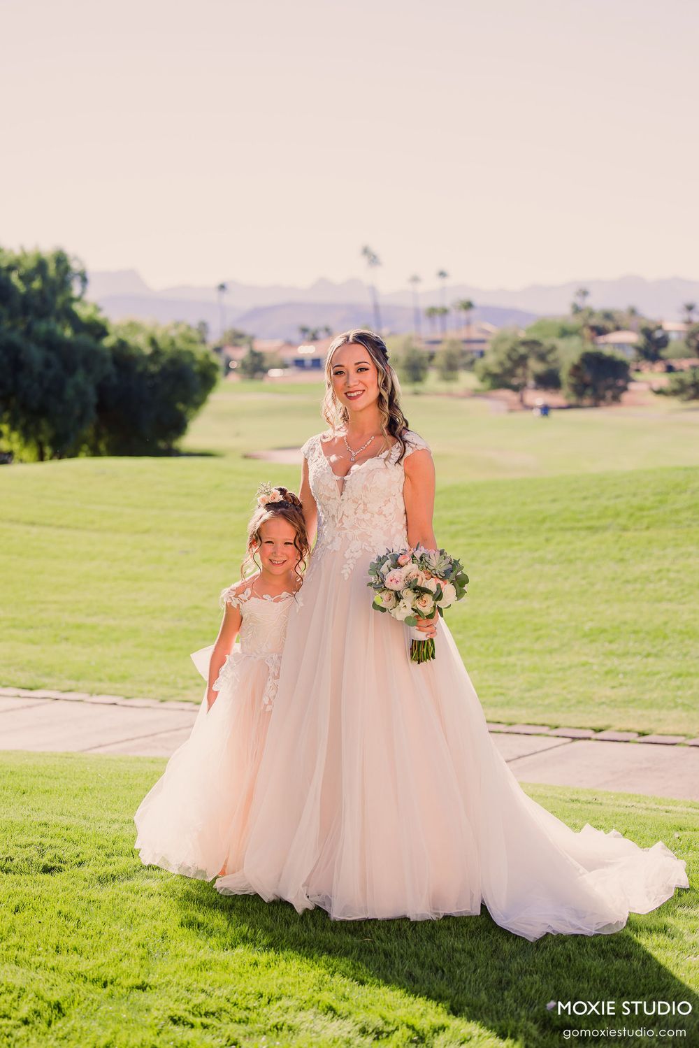 Beautiful wedding scene on a sunny golf course with matching white dresses and a floral bouquet.