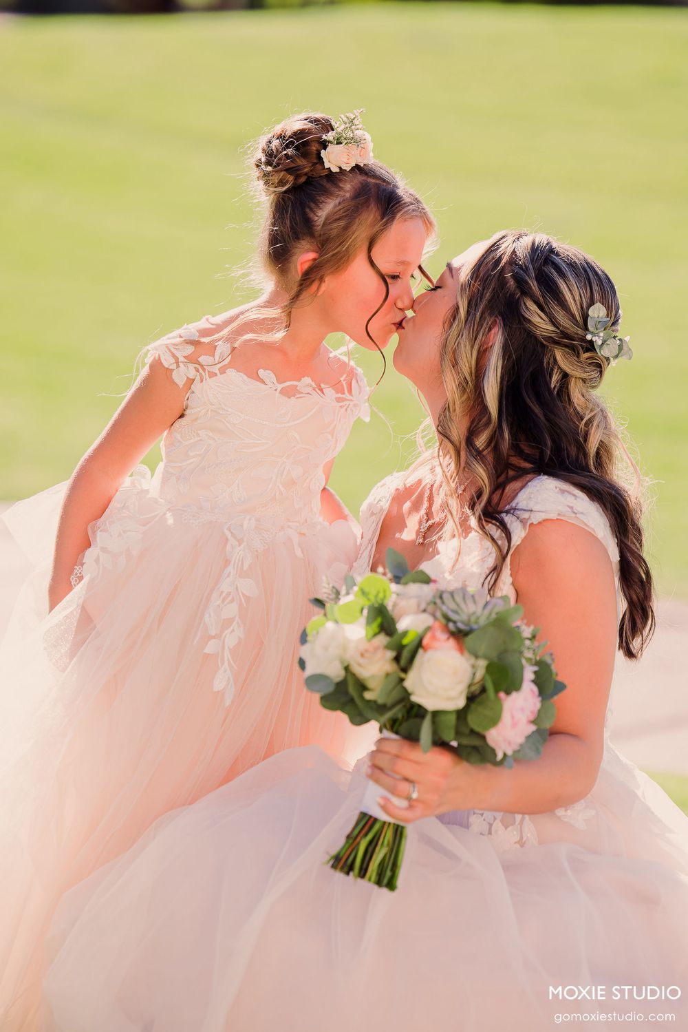 Wedding party members in coral pink dresses share a joyful moment together on a sunny outdoor lawn.