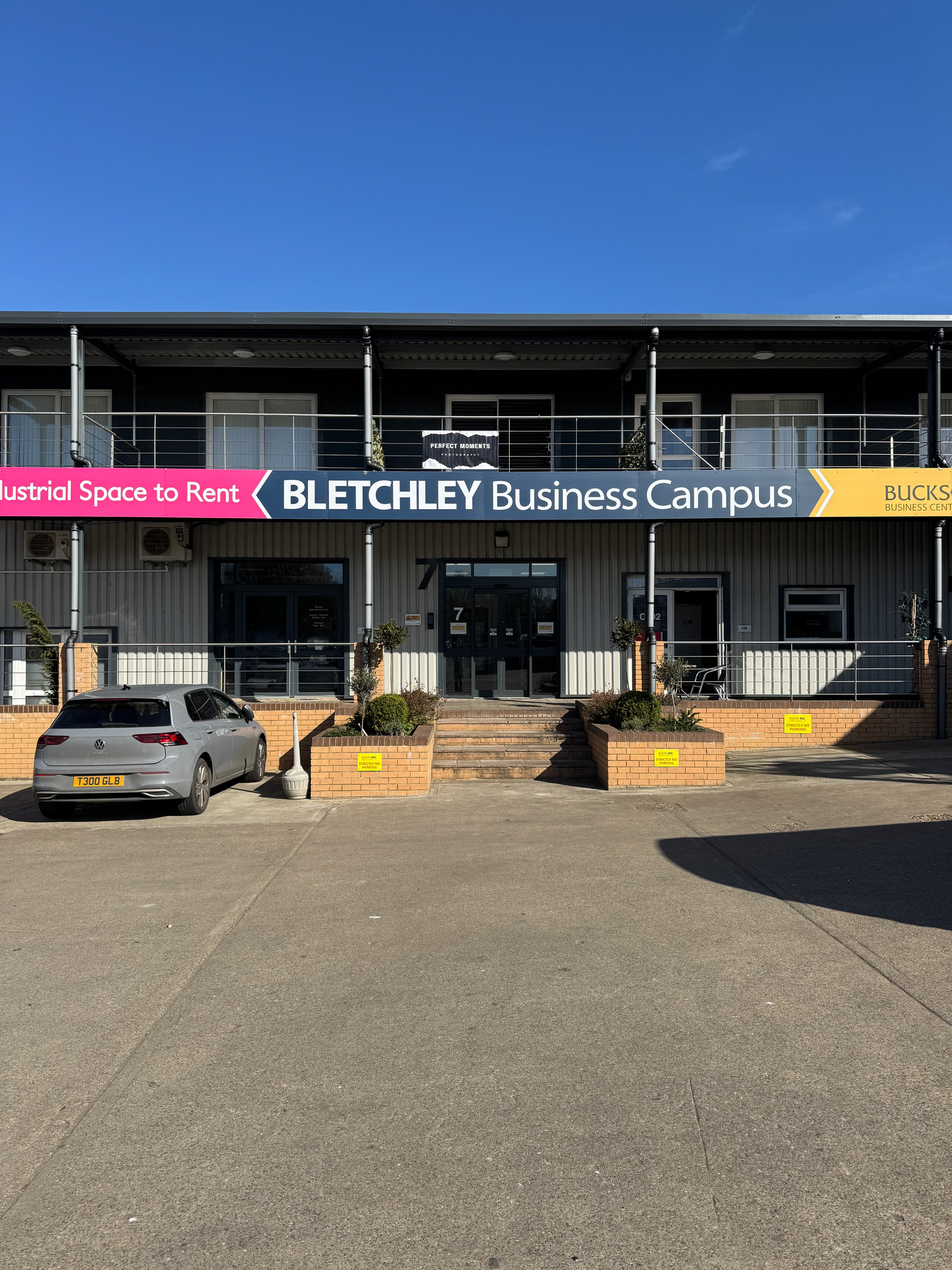 Exterior view of Bletchley Business Campus building entrance with signage and parked car on a sunny day.