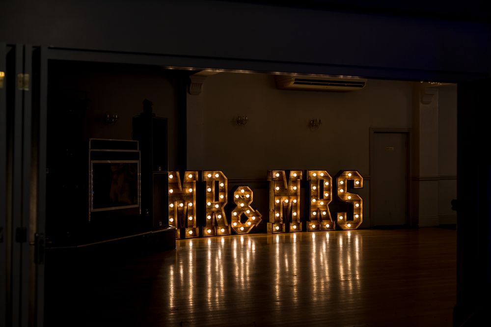 Illuminated 'MR & MRS' sign creating a romantic ambiance in dark reception venue.
