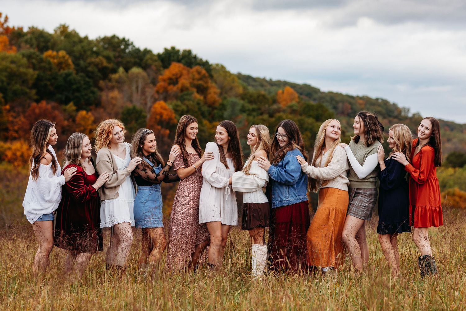 Group of young women in fall sweaters and boots posing in a scenic autumn foliage field.