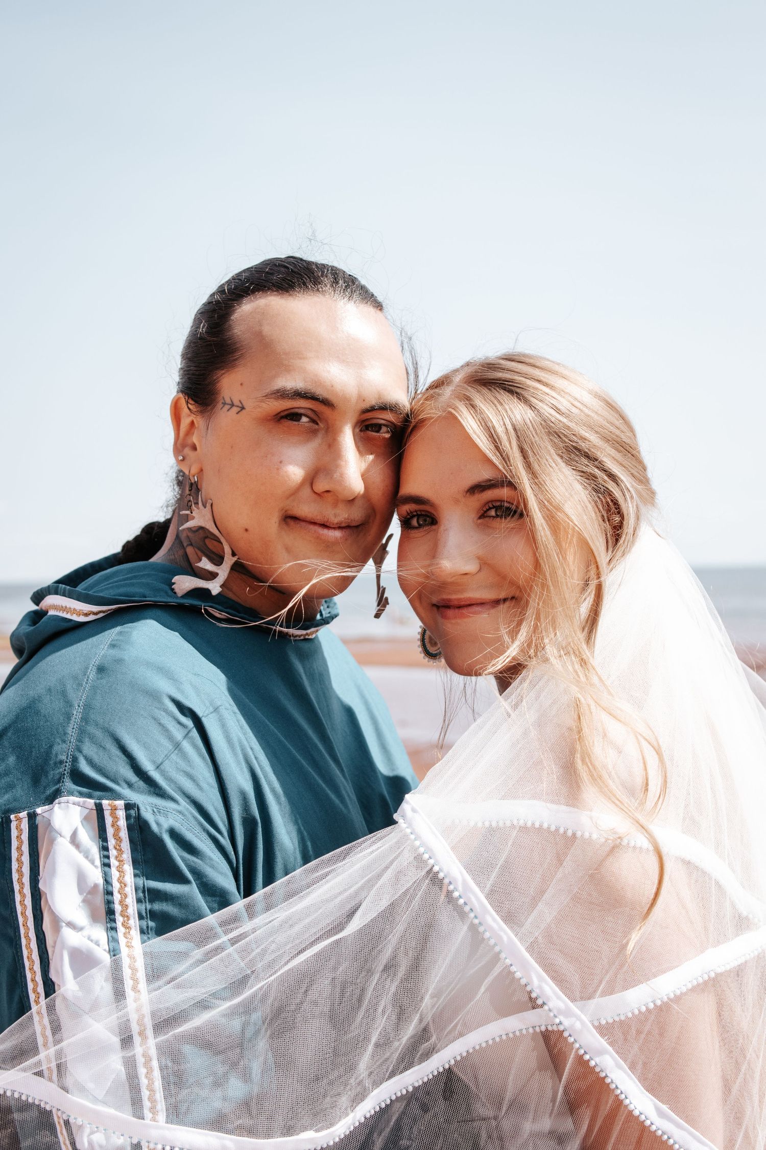 A couple embraces on their wedding day with a white veil flowing in the breeze. Photo at Charlottetown PE