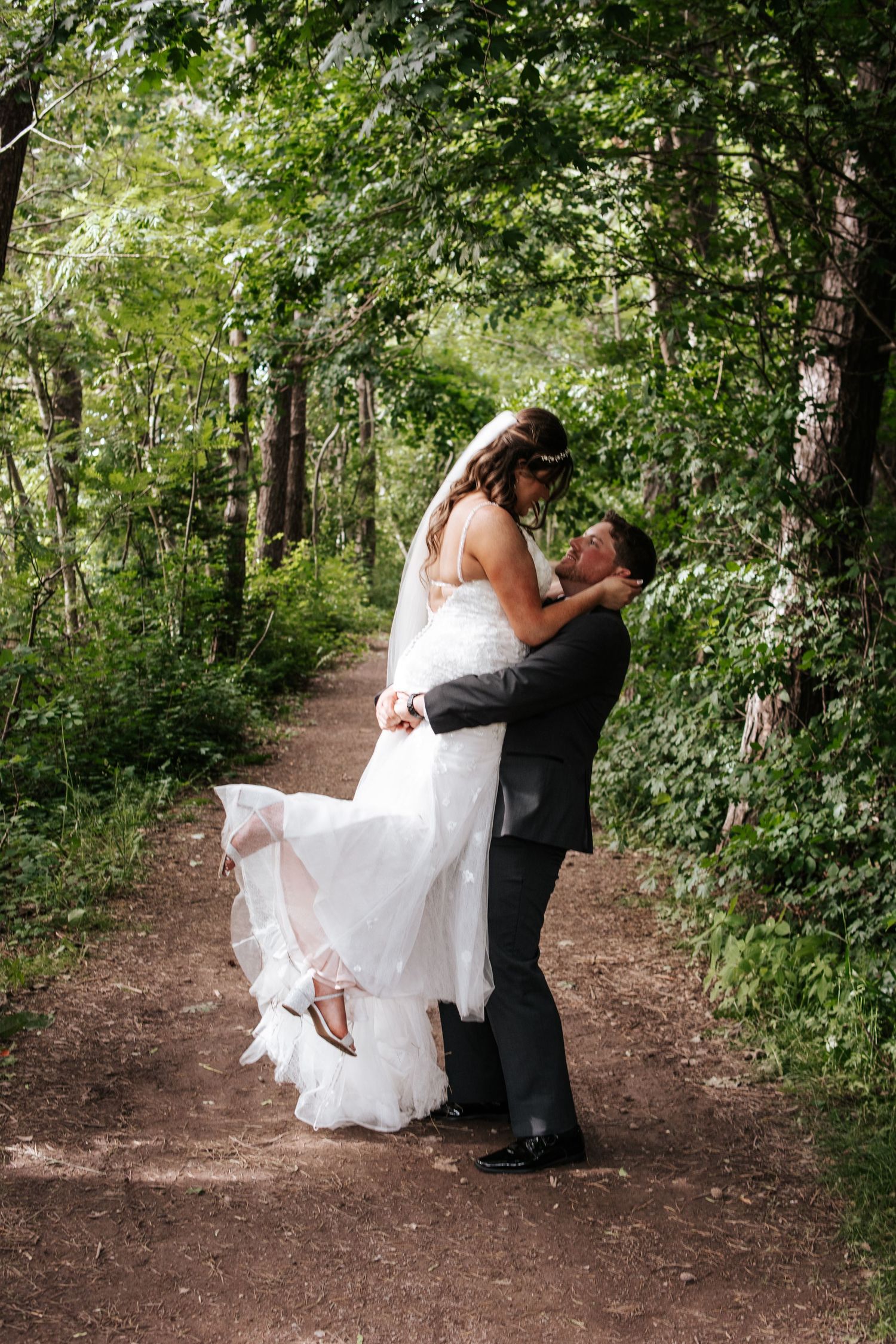 A groom lifts his bride on a forest path during their wedding photoshoot. Photo at Charlottetown PE