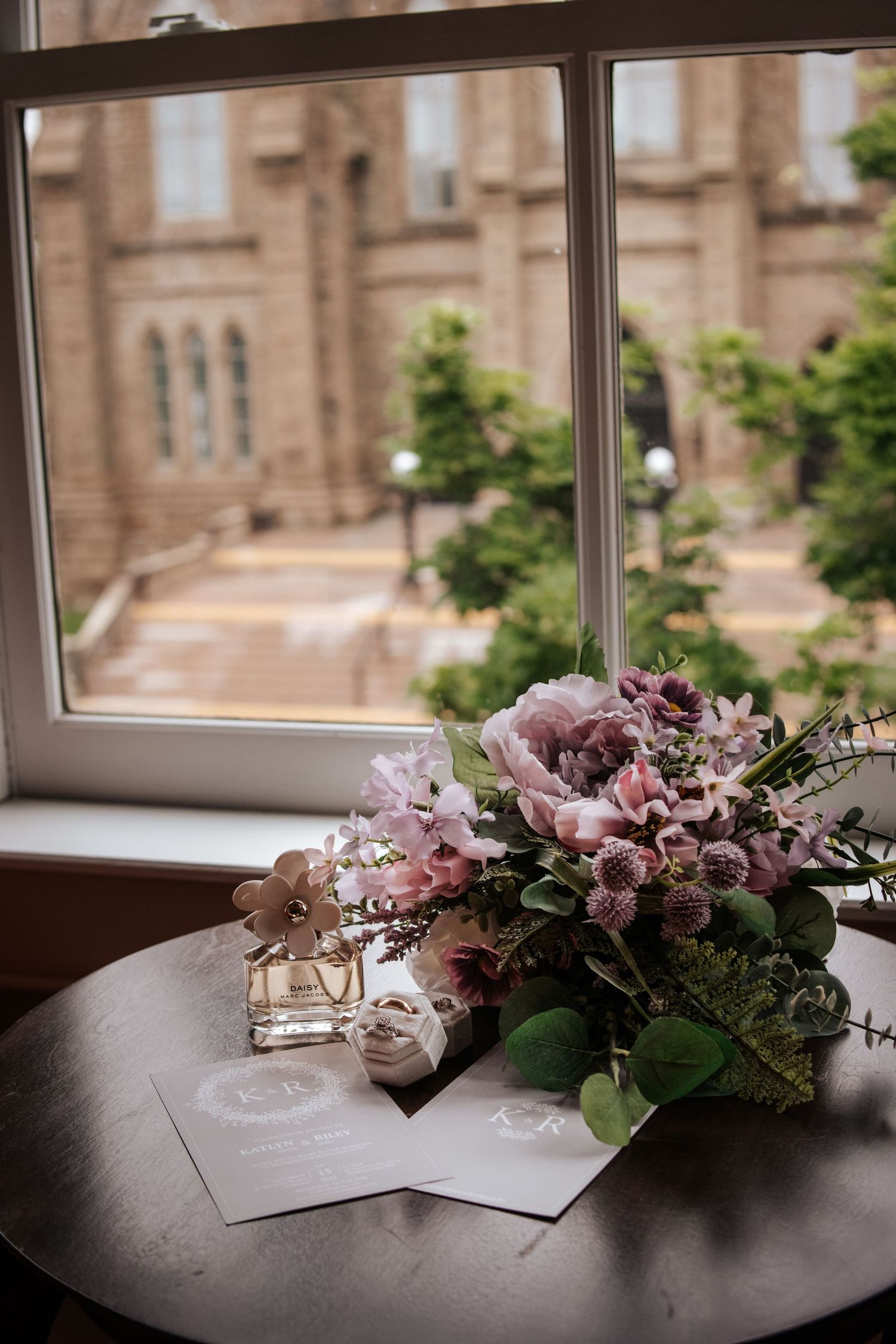 Pink floral arrangement with wedding invitations on wooden table by church window. Photo of St Dunstan's Basilica PEI