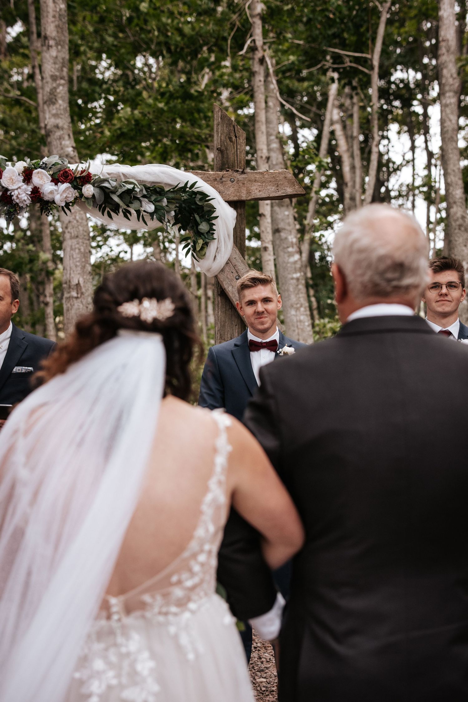 Wedding ceremony setup in woods with floral arch and guests gathering. Photo at Clinton Hills PEI