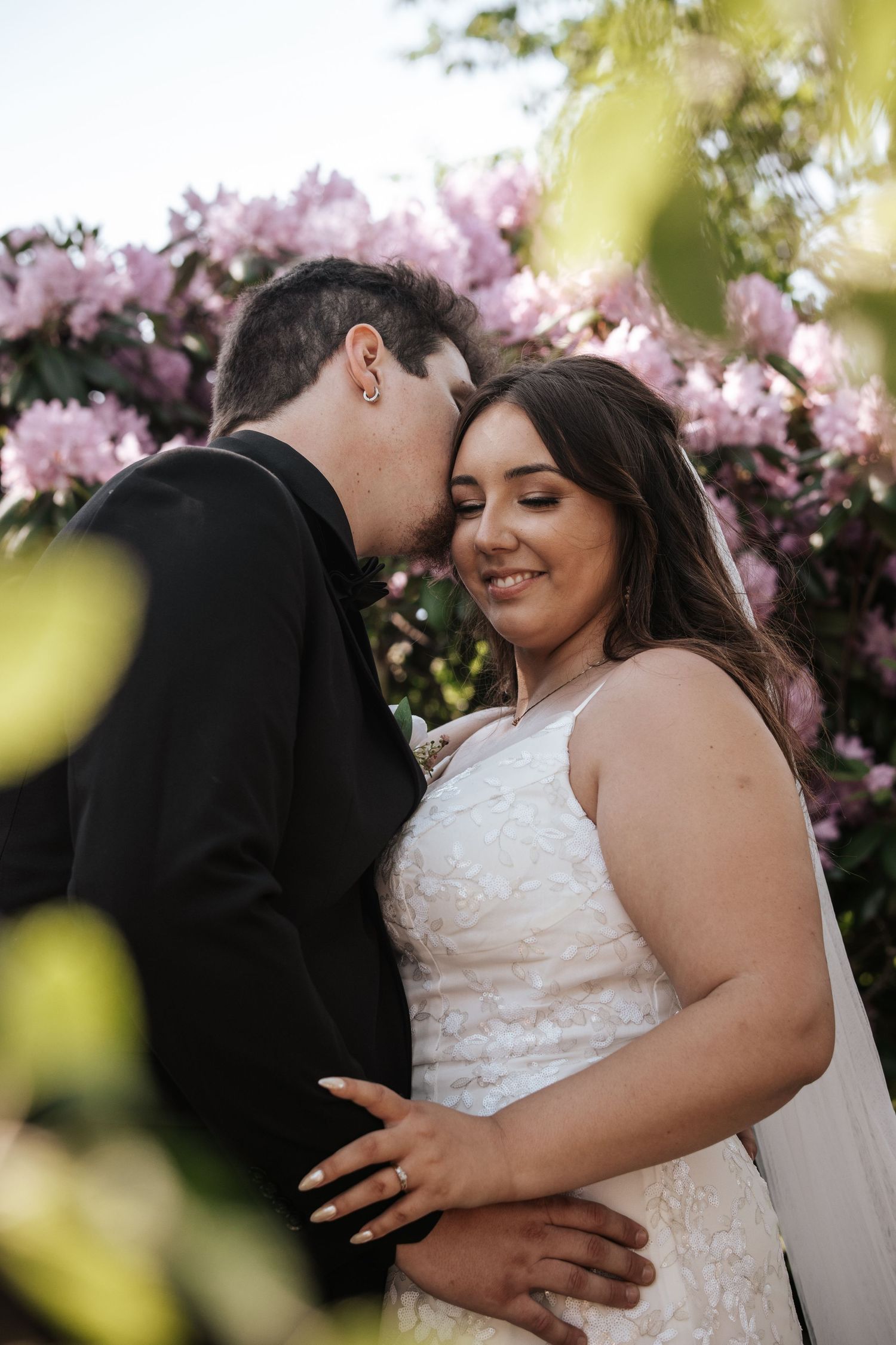 A romantic wedding moment captured under blooming pink cherry blossoms with a couple embracing. Photo at Montague PEI
