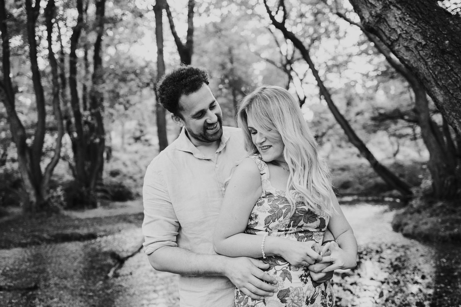A romantic black and white photo of a couple sharing a joyful moment together in a wooded outdoor setting.