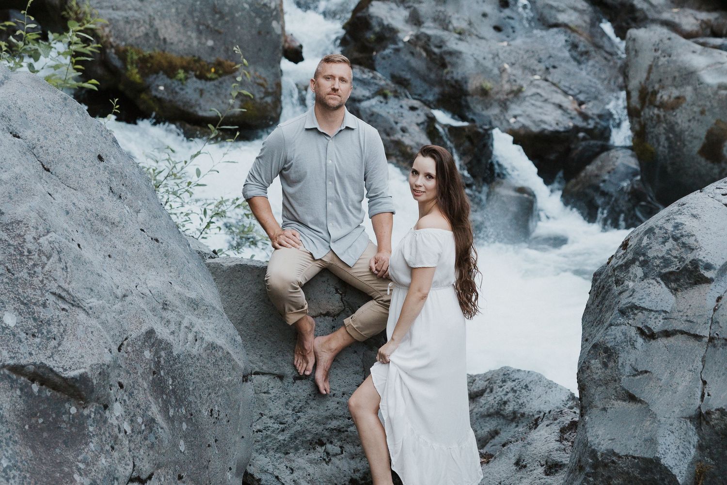 Couple sitting together on rocky terrain near a cascading waterfall.