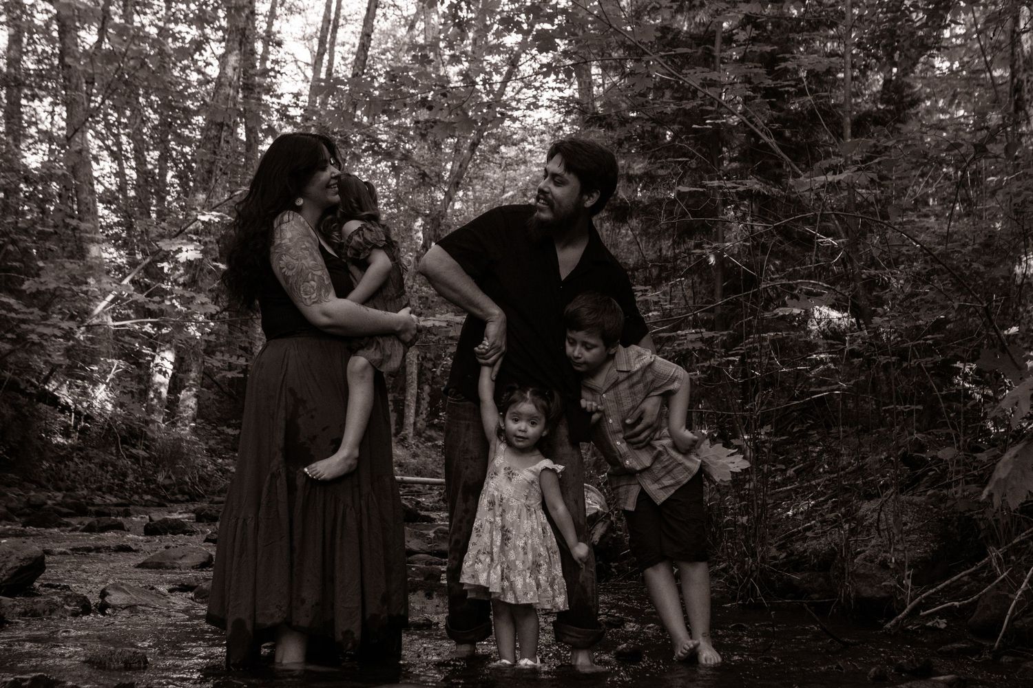 A young couple and their three children stand in a creek photographed in black and white.