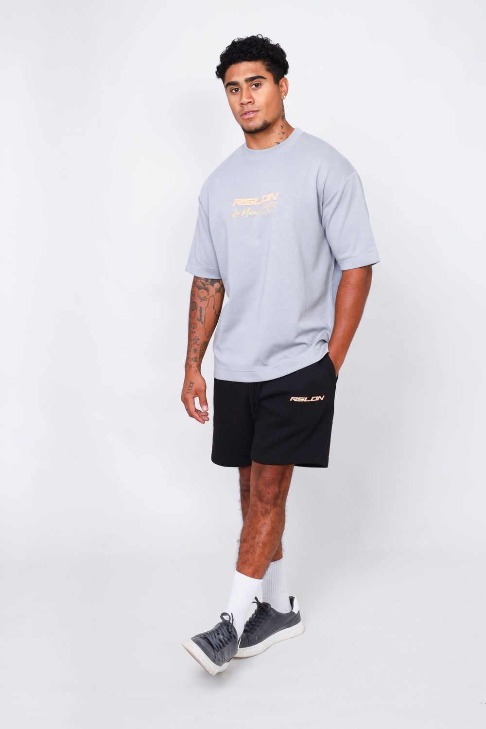 Young man in casual grey t-shirt and black shorts showing full body fashion look.