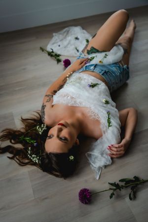 A woman lying on a wooden floor covered in white lace and denim shorts surrounded by scattered wild flowers at The White Space Las Vegas.