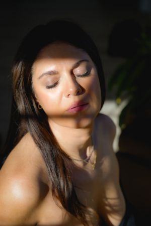 Portrait in dramatic natural lighting with soft shadows and plant decor.