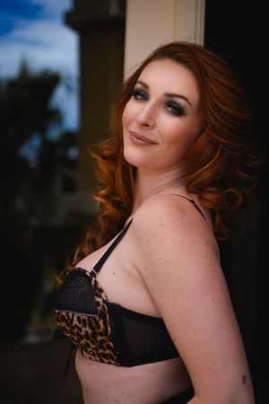 Portrait with curled red hair wearing a black and leopard print bra in an outdoor setting with soft lighting.
