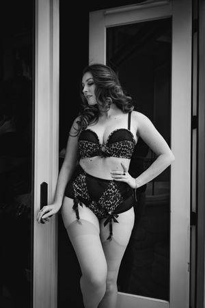Black and white boudoir photograph featuring feminine lingerie with lace details in a doorway setting.