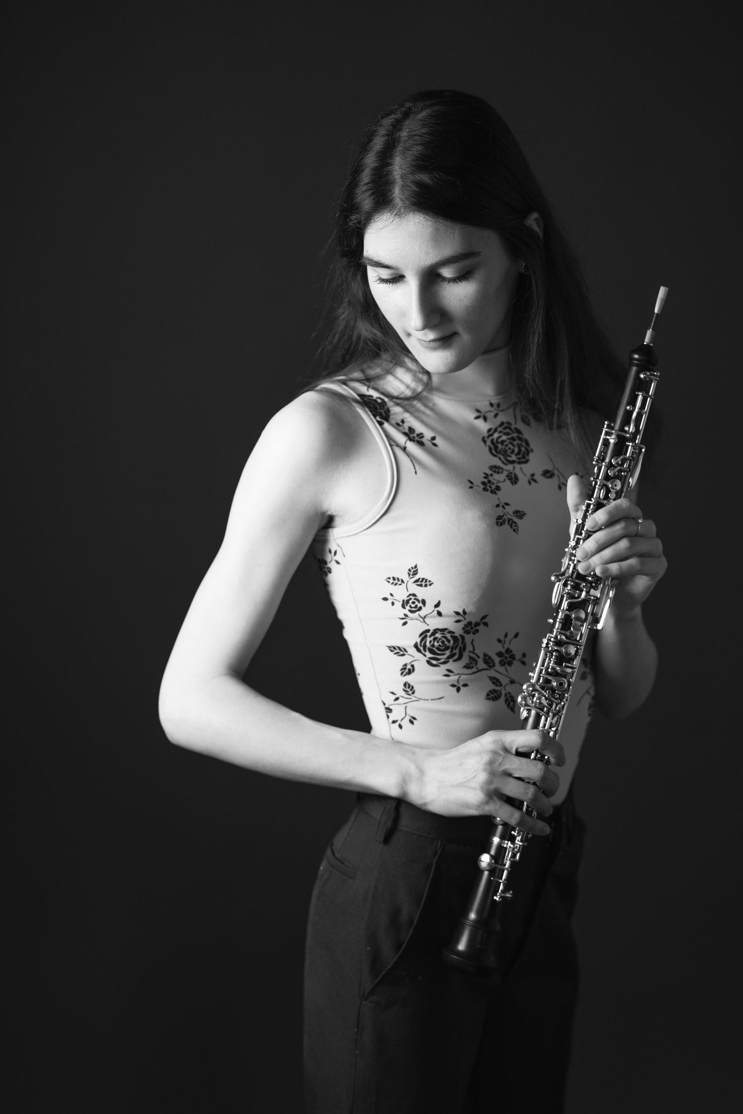 Artistic black and white photo of musician holding oboe against dark background.
