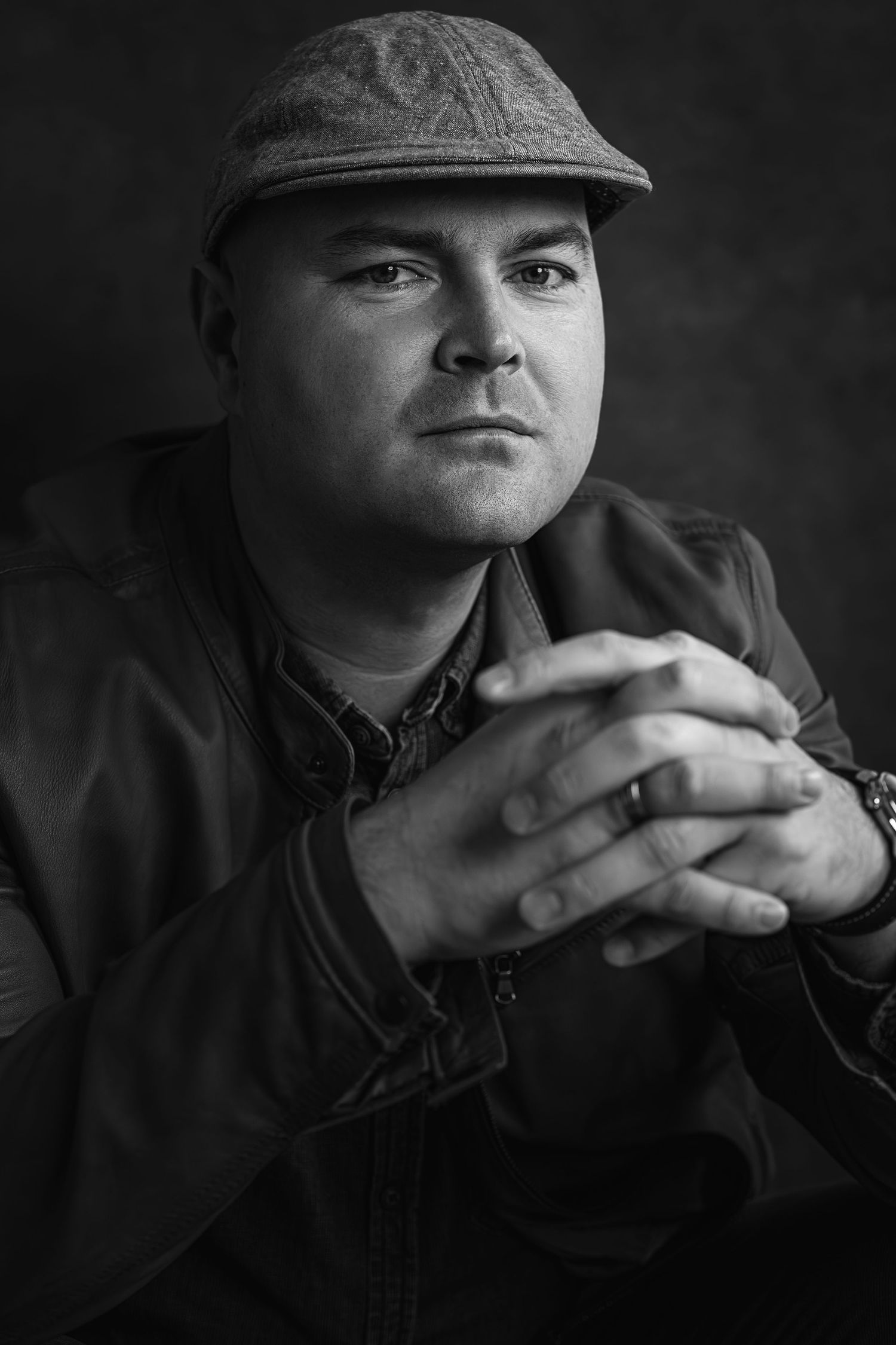 Black and white portrait of a person wearing a flat cap and casual jacket.