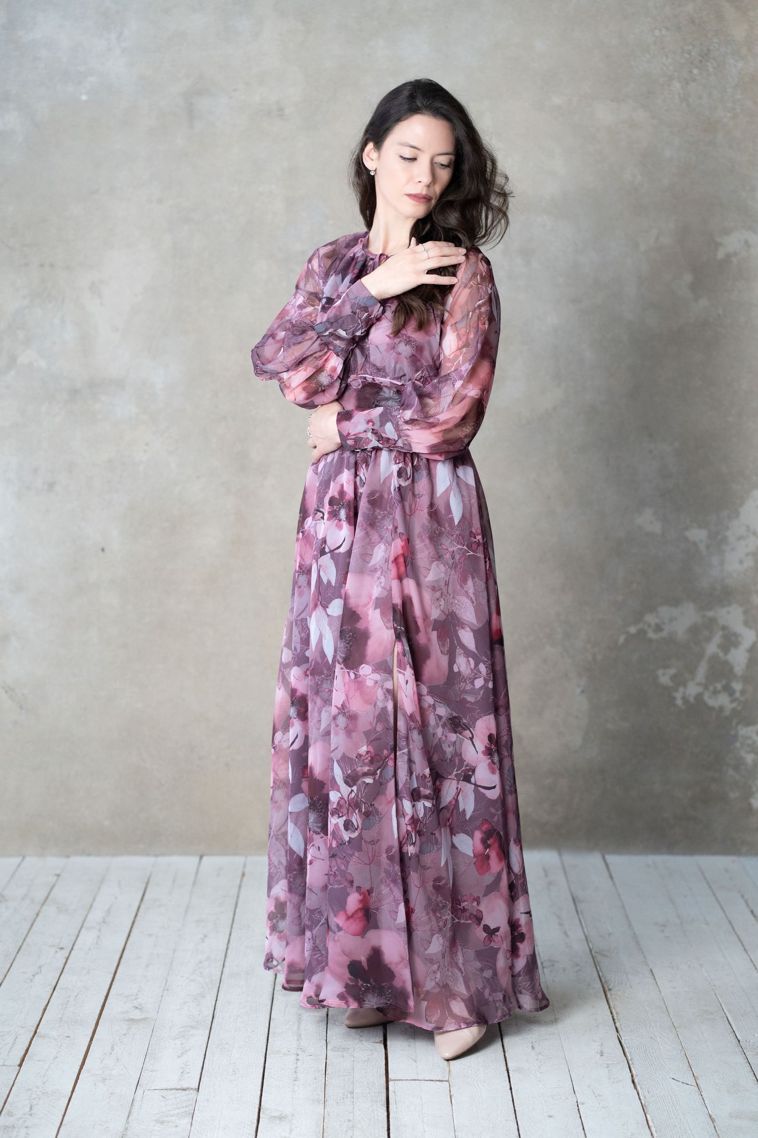 Romantic floral maxi dress in shades of purple and pink shown on a simple studio backdrop with wooden floor.