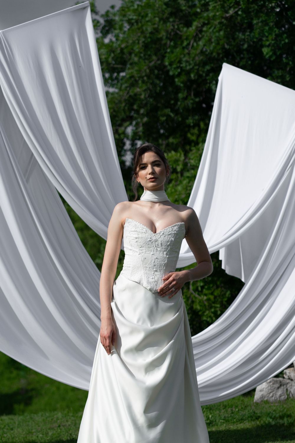 White flowing drapery creates an elegant outdoor backdrop against lush green foliage for a wedding photo shoot.