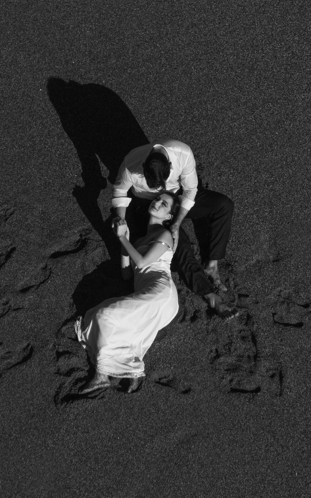 Romantic black and white beach scene of couple embracing on sandy shore.
