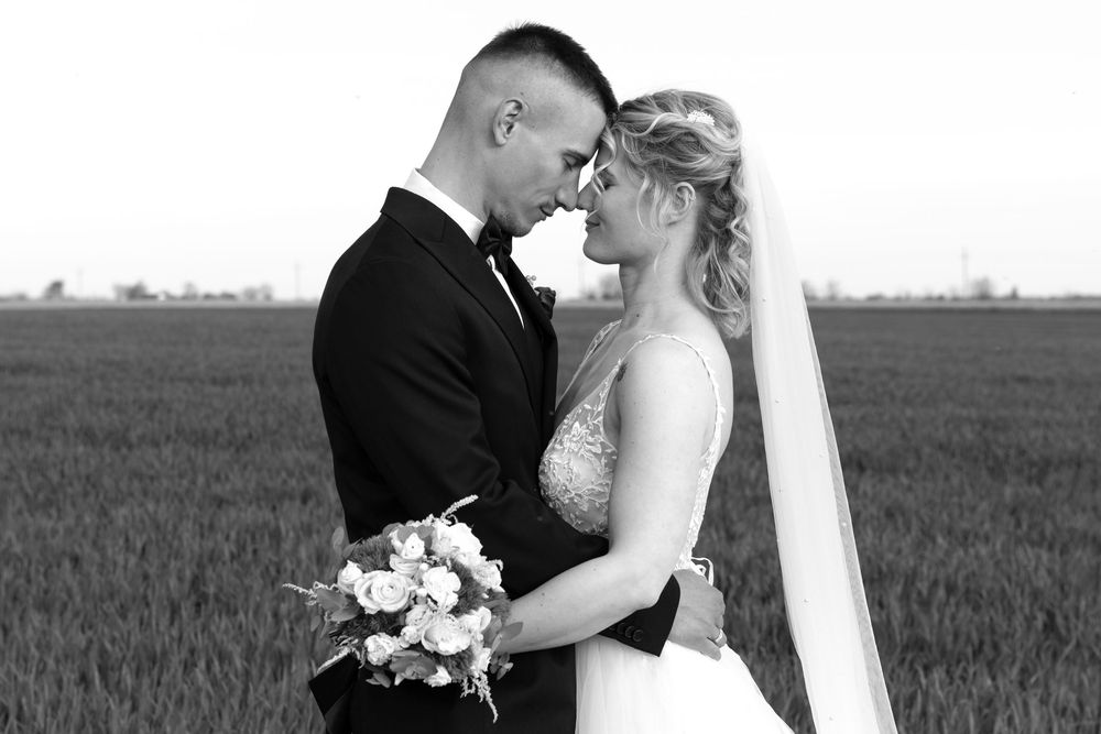 Romantic black and white wedding portrait of couple embracing in field.
