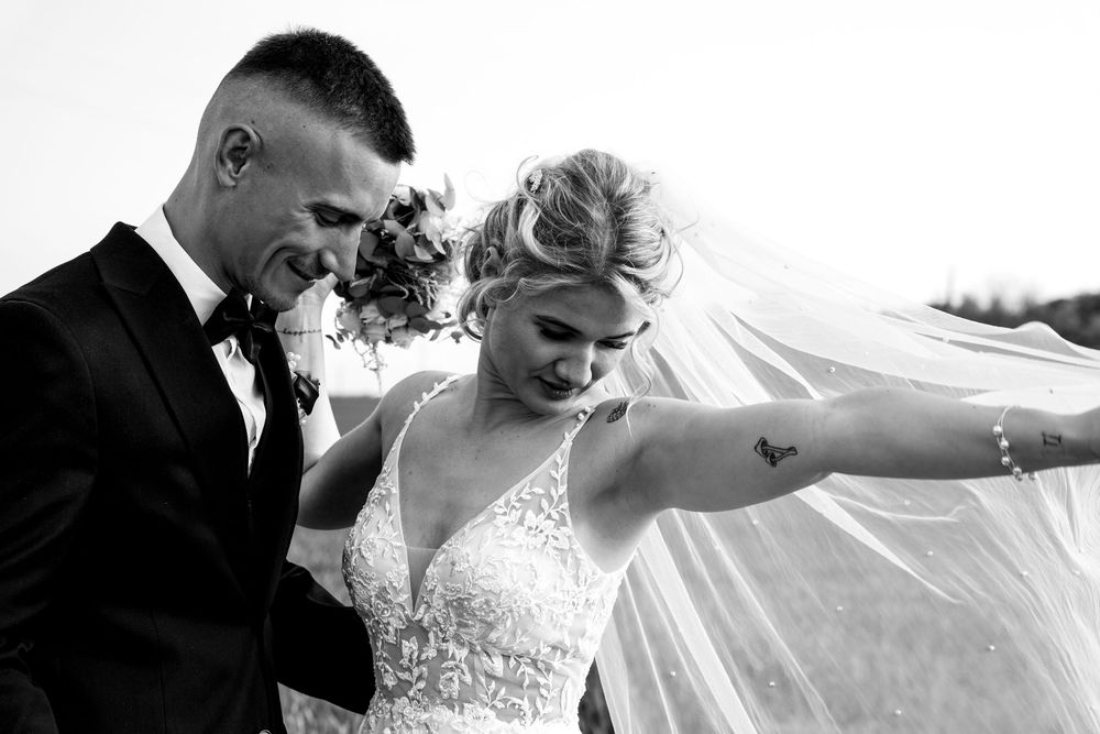 Wedding couple sharing playful moment with bride's veil in black and white.