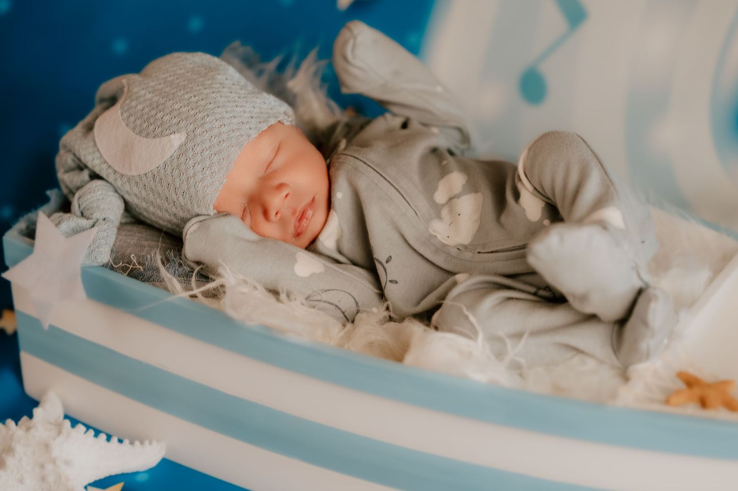 Sleeping baby wearing knit bonnet and sweater rests on gray cushion.