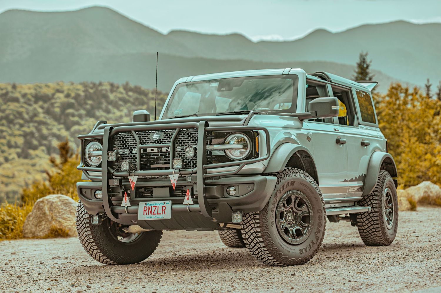 Close-up view of a rugged off-road vehicle's front bumper and grille against a mountainous backdrop.