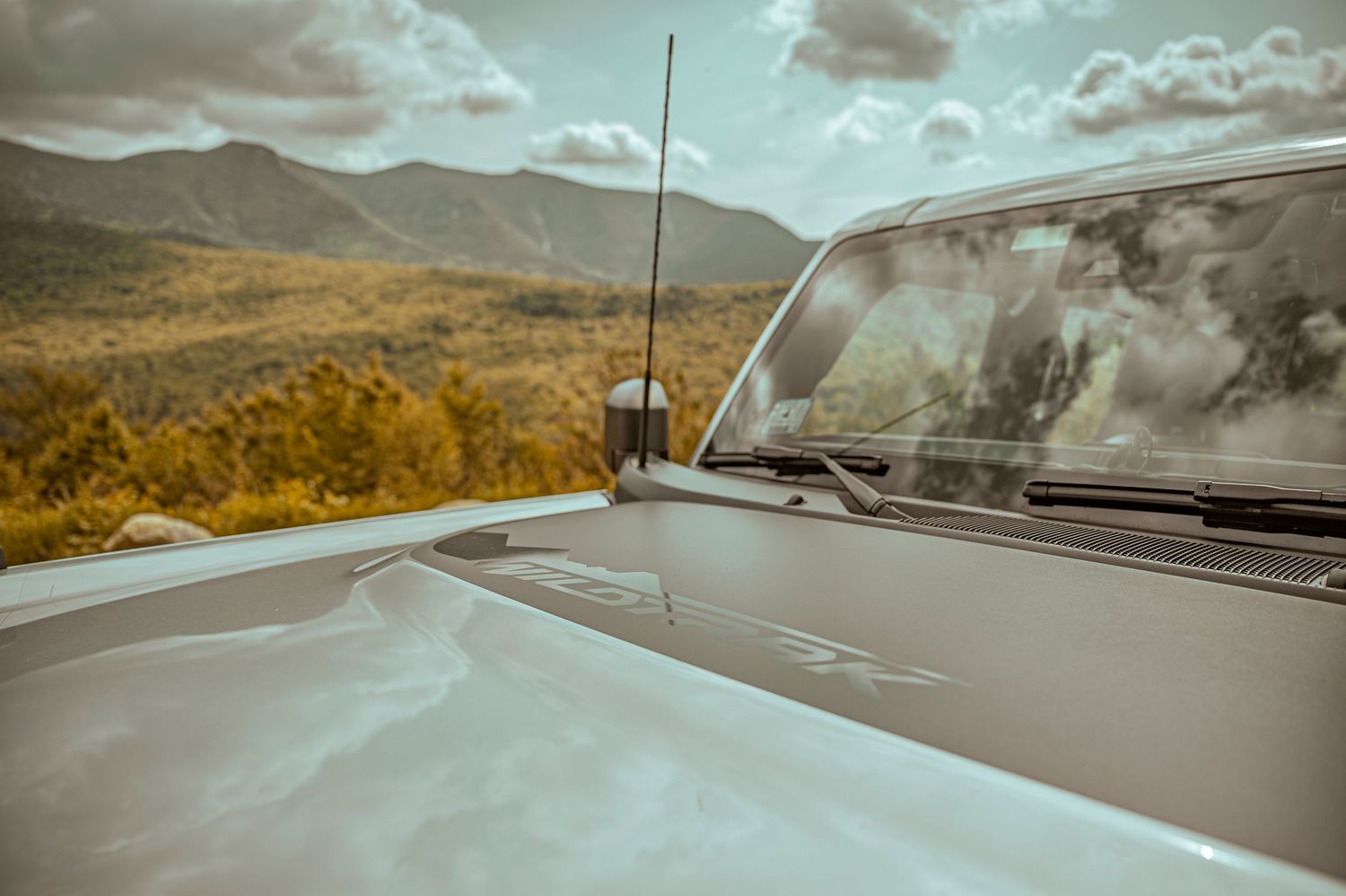 A scenic mountain road stretches into the distance with dramatic cloudy skies and rolling hills in autumn colors.
