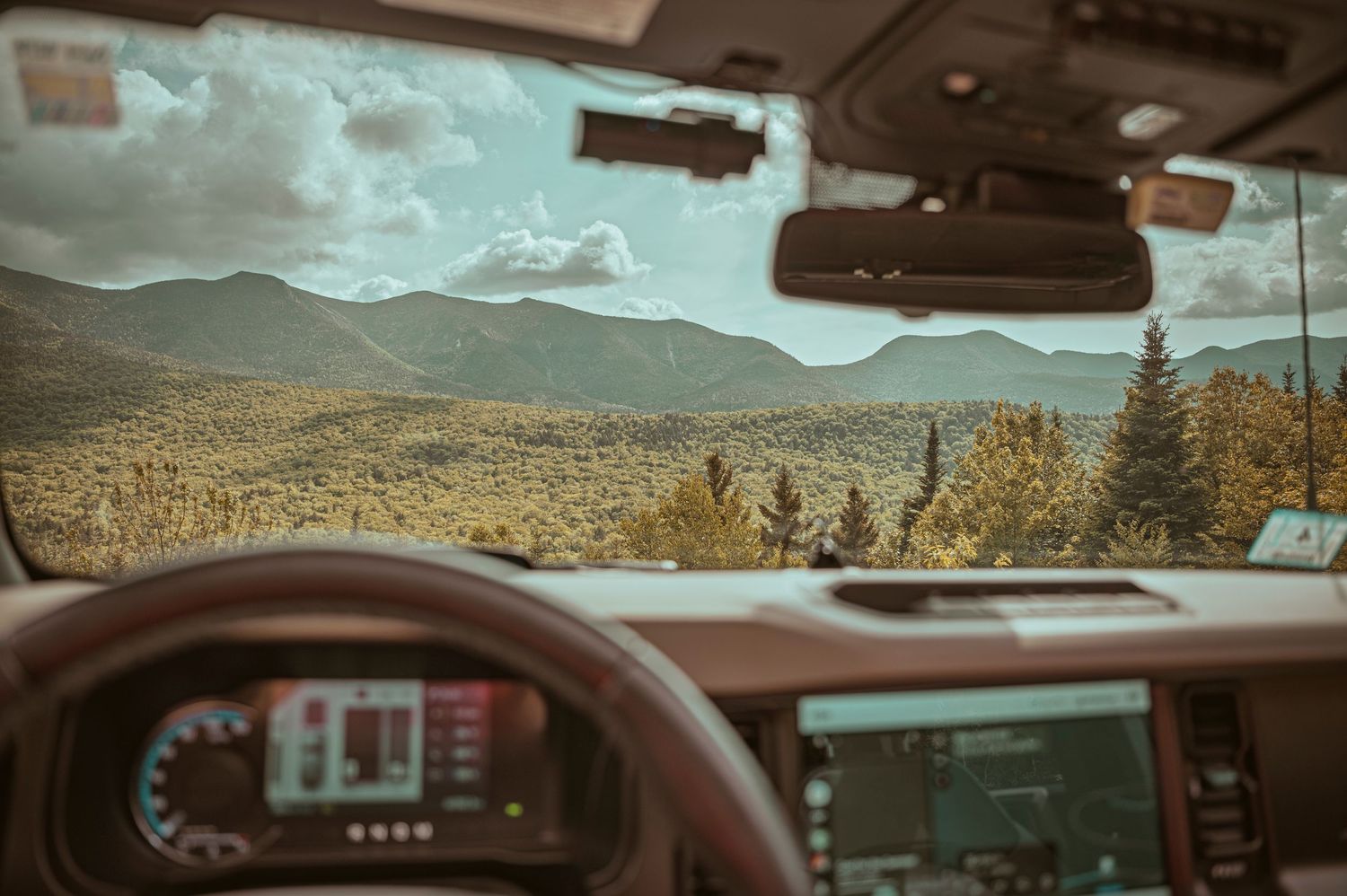 Dashboard view through a car windshield showing a winding mountain road ahead with scenic fall landscape.