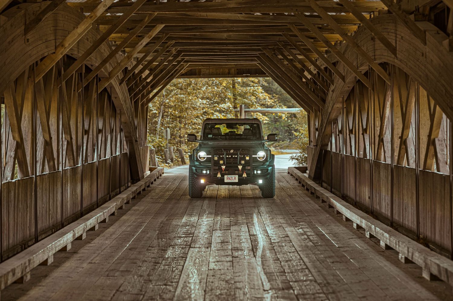Vintage truck drives through a long wooden covered bridge with sunlight streaming through the slats.