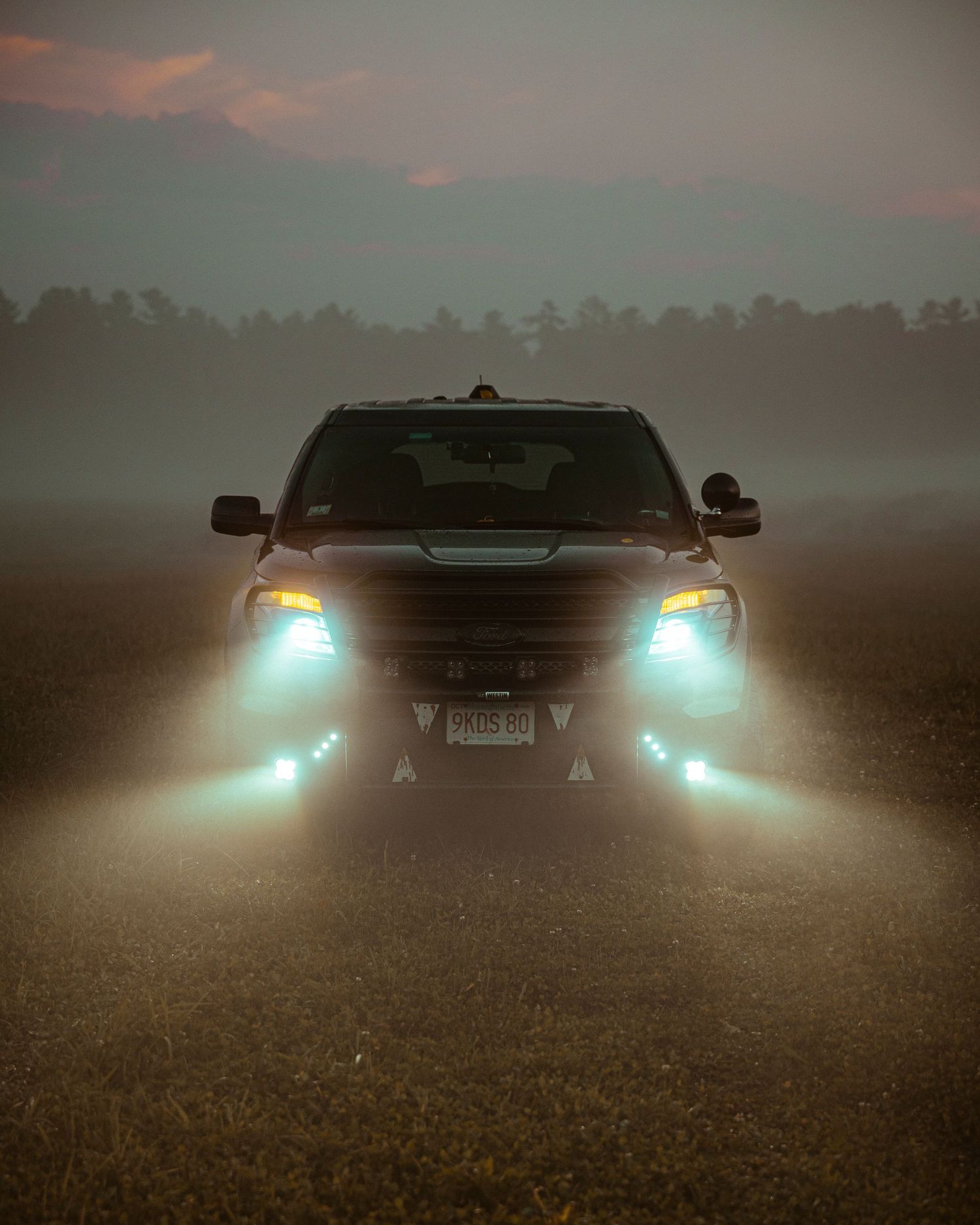 Vehicle with glowing headlights creates dramatic silhouette against misty forest backdrop.
