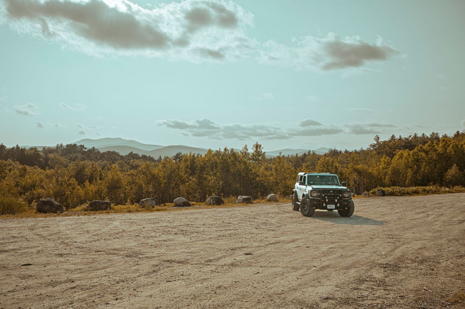 A vintage turquoise car parked in a desert landscape with mountains and golden trees in the background.