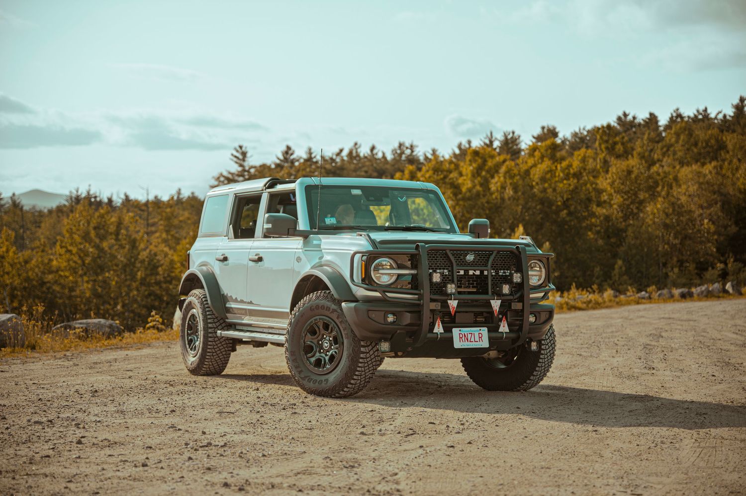 Lifted off-road vehicle with rugged tires and custom modifications parked in a desert landscape at sunset.
