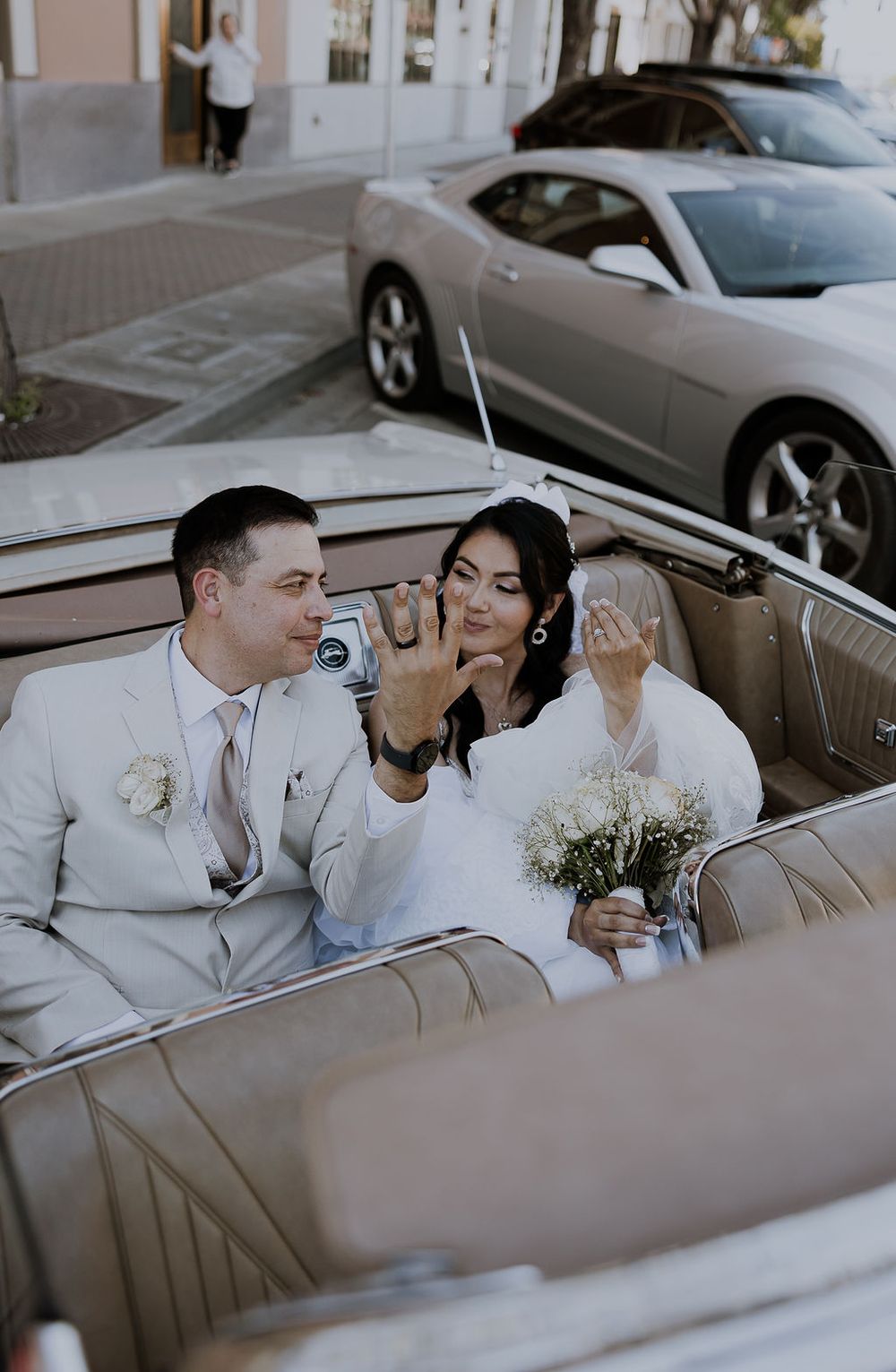 A couple shares an intimate moment in a classic convertible car on their wedding day.
