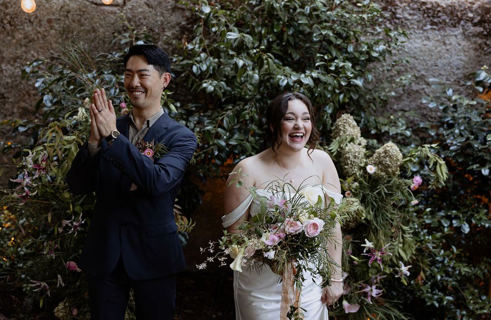 A wedding ceremony unfolds in a garden setting with lush floral arrangements and greenery.