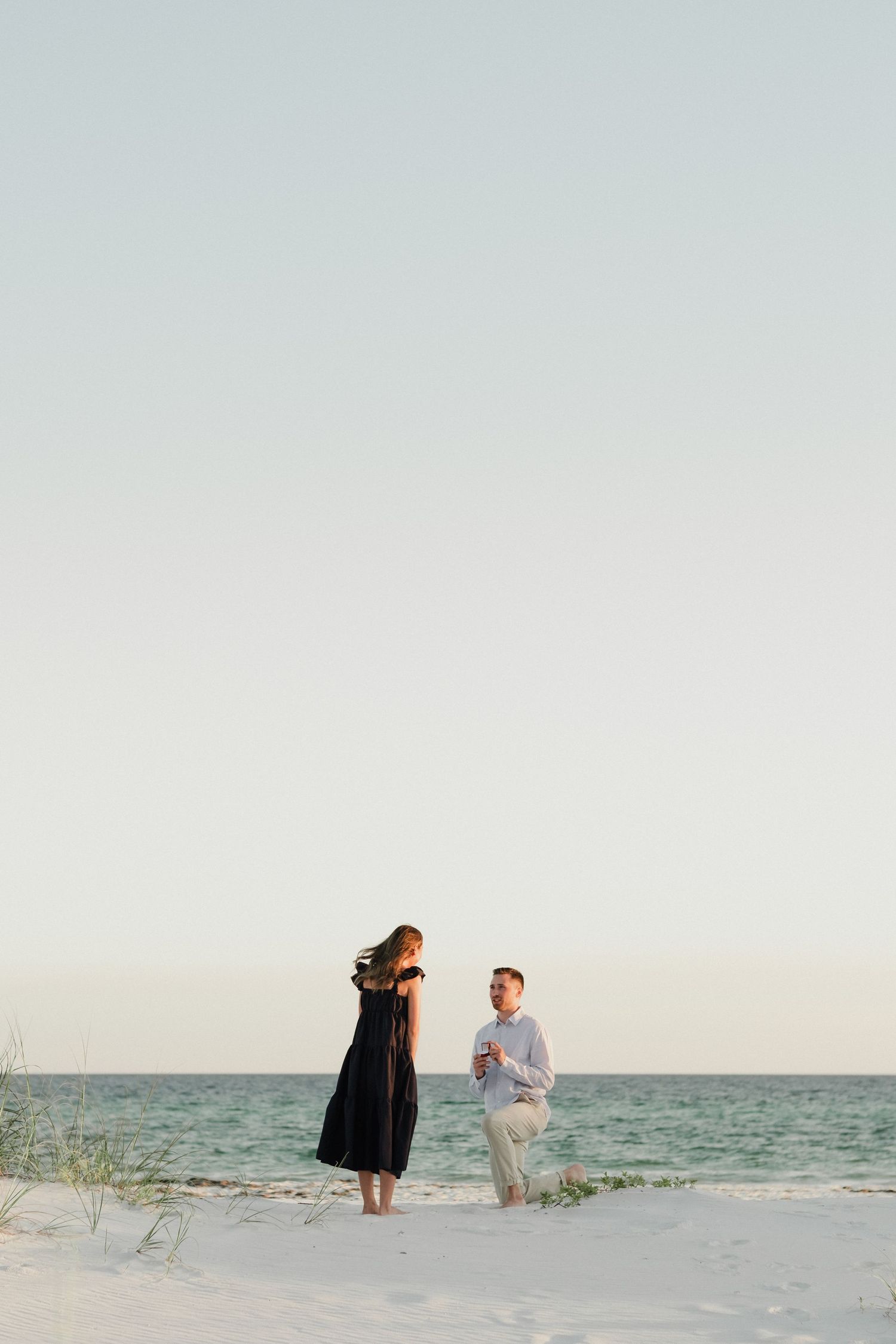 Couple shares intimate moment on white sandy beach with ocean view.