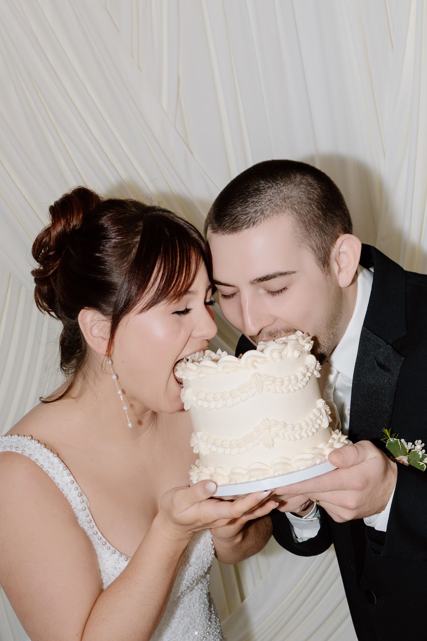 Bride and groom joyfully eating their white tiered wedding cake together at their wedding reception.