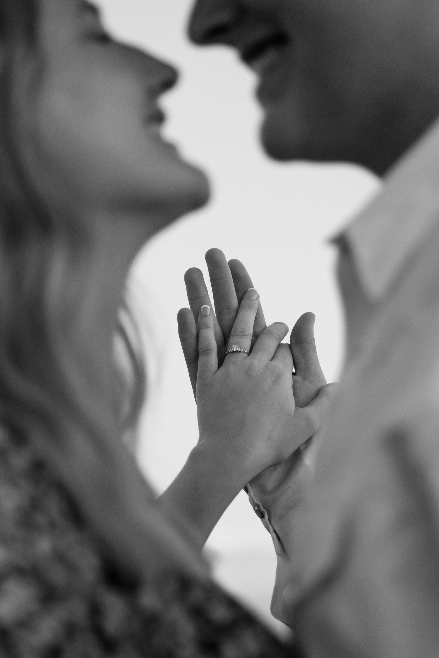 Black and white close-up of couple nearly kissing while holding hands showing engagement ring.