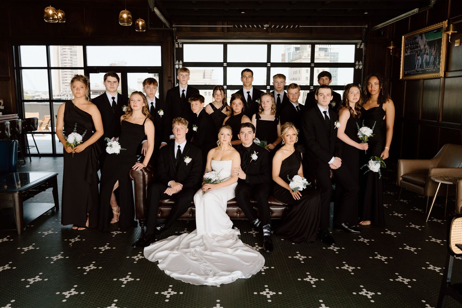 Large wedding party dressed in black poses together in an elegant dark-themed venue.