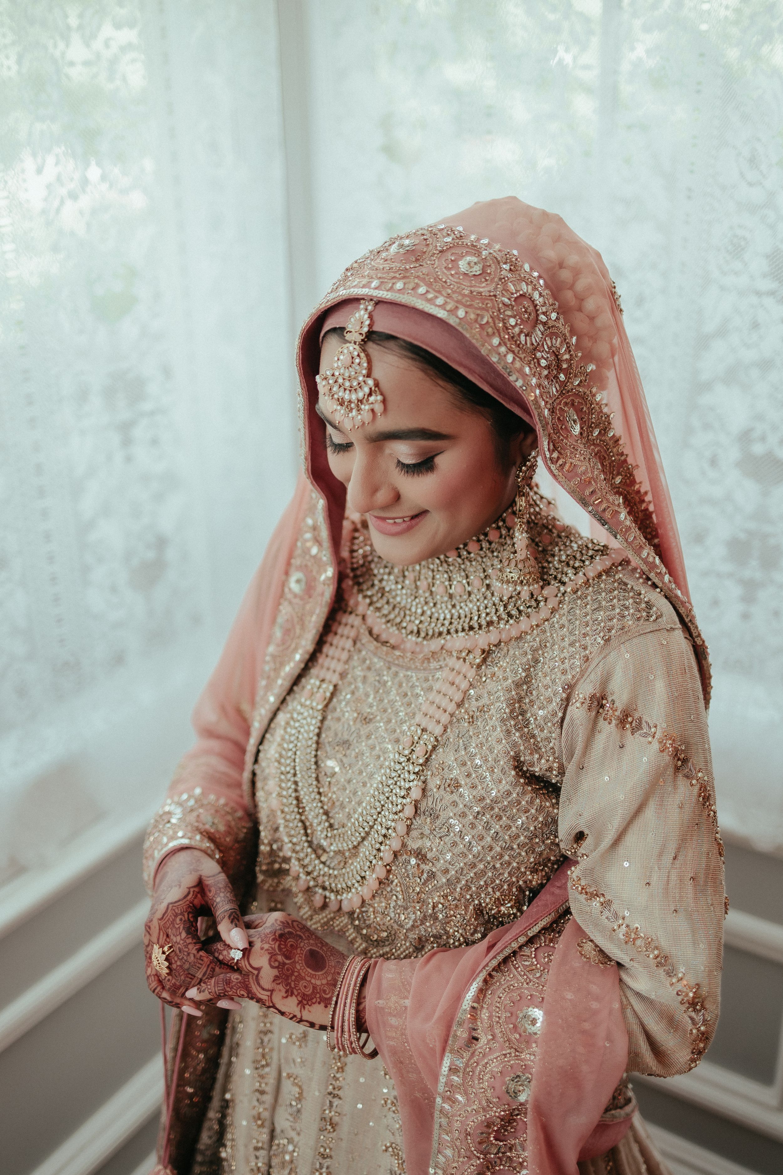 Traditional South Asian bride wearing ornate pink and gold wedding attire with detailed jewelry.